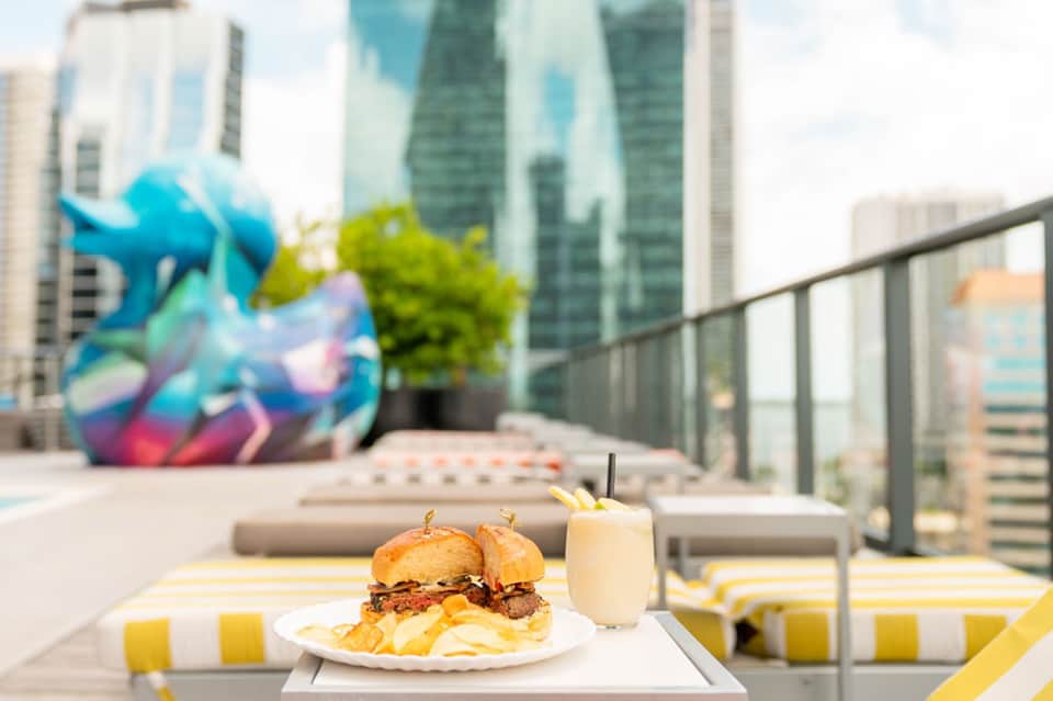 Rooftop dining with gourmet burger and drink overlooking city skyline and colorful art installation