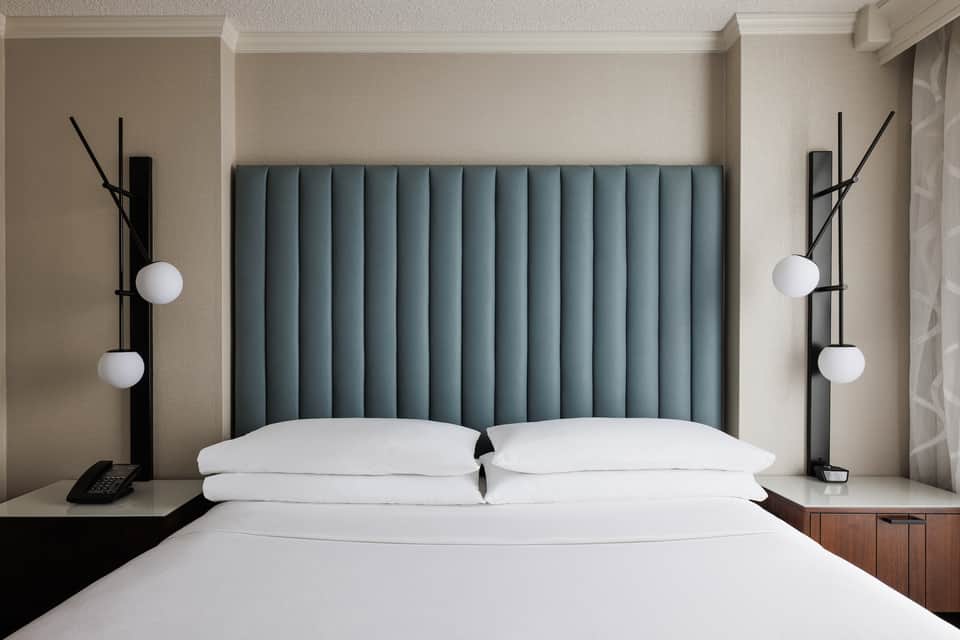 Modern hotel bedroom with teal upholstered headboard, white pillows, and contemporary black bedside lamps