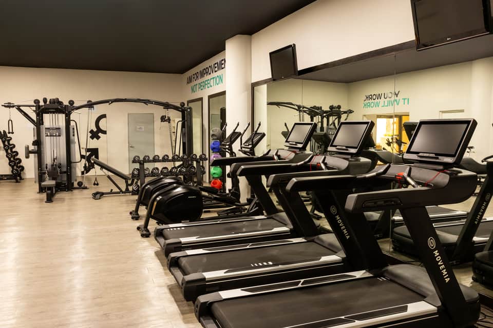 Spacious gym with treadmills, stationary bikes, multi-station equipment, and wall-mounted screens