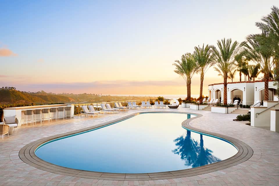 Luxury resort infinity pool with ocean view at sunset, palm trees, and white architectural structures