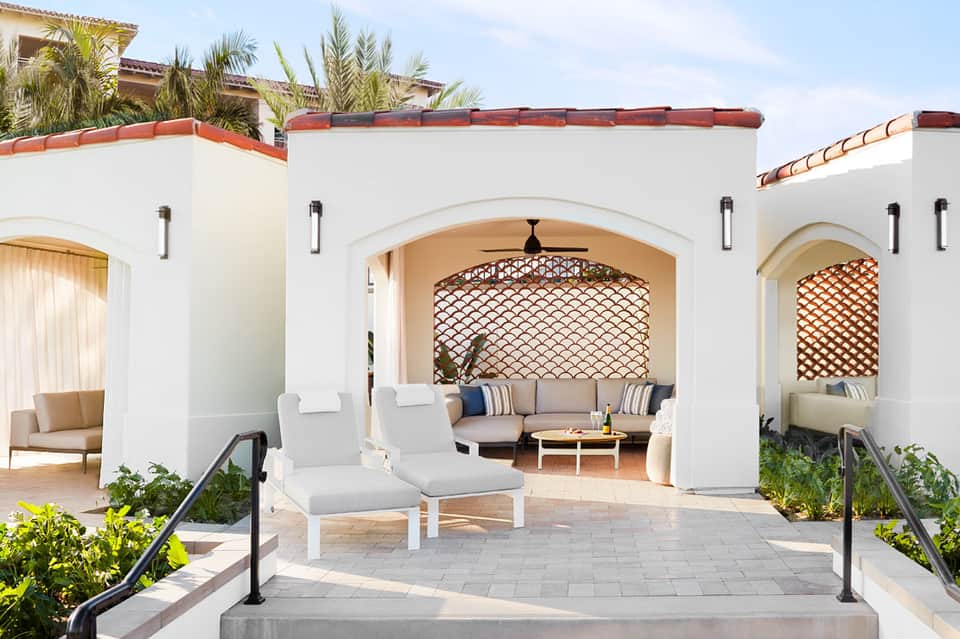 Mediterranean-style resort courtyard with white arches, lounge seating, and palm trees