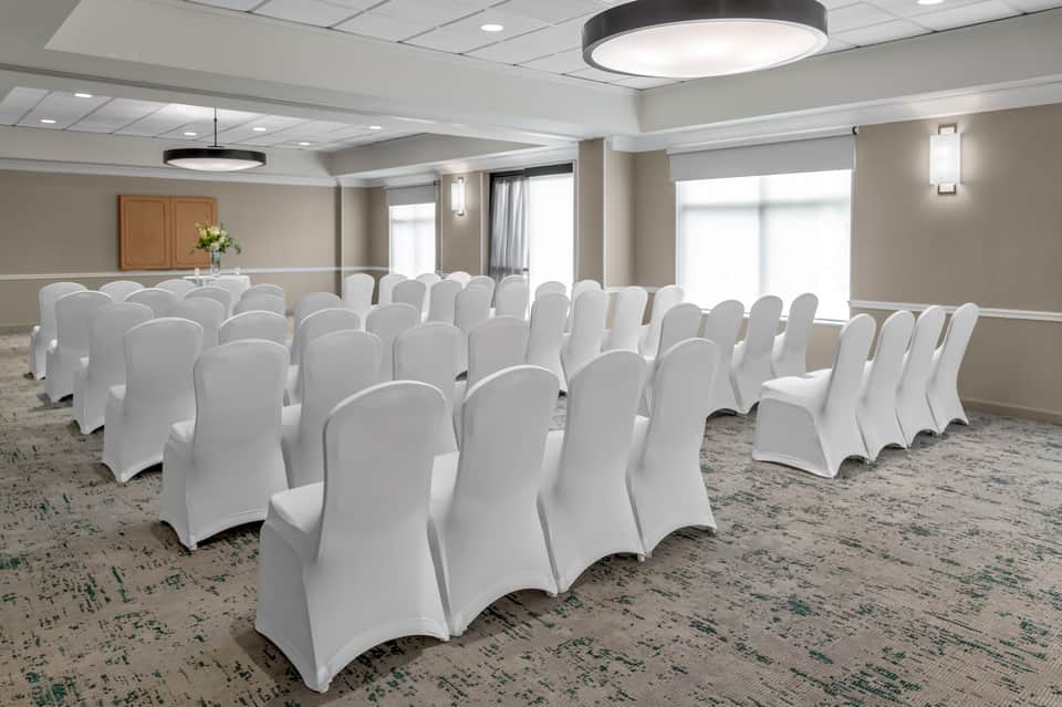 Meeting space with white chair covers arranged in rows and windows with drapes