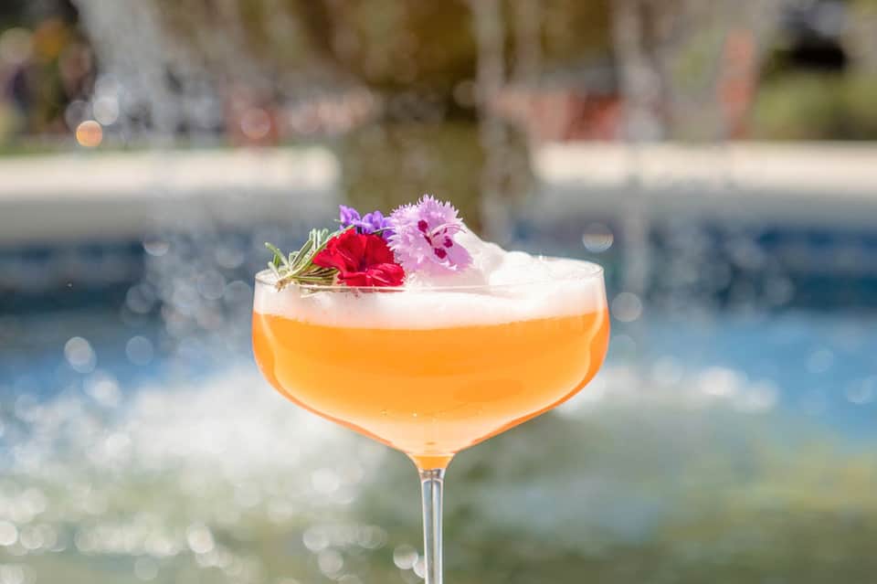Elegant cocktail with orange liqueur and edible flowers by poolside
