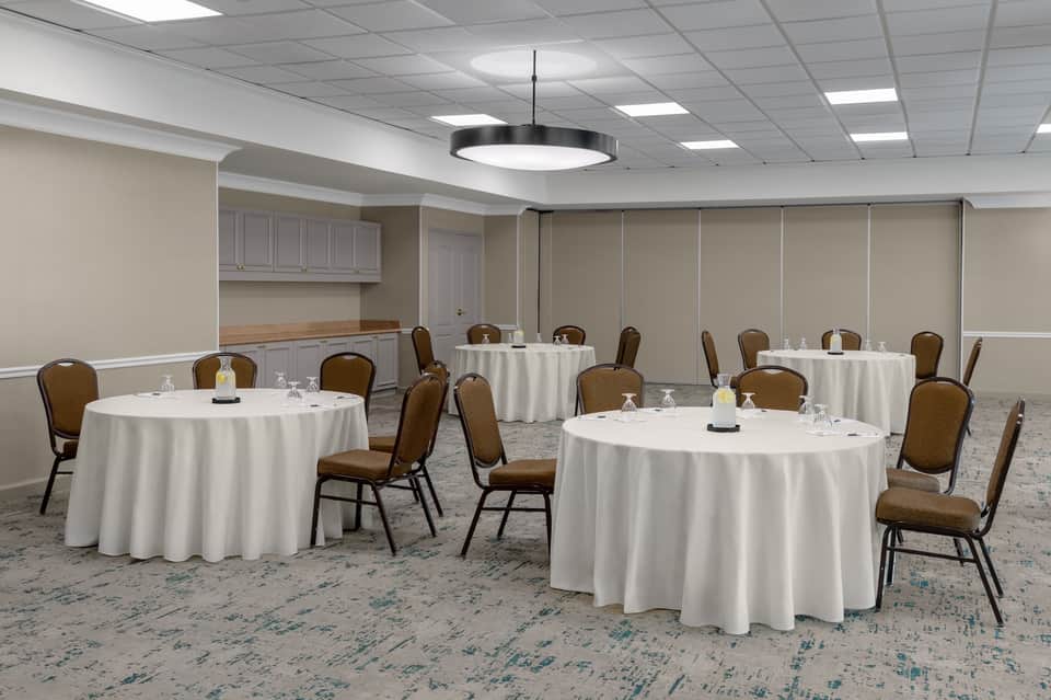 Banquet room with multiple round tables draped in white linens and brown stacking chairs