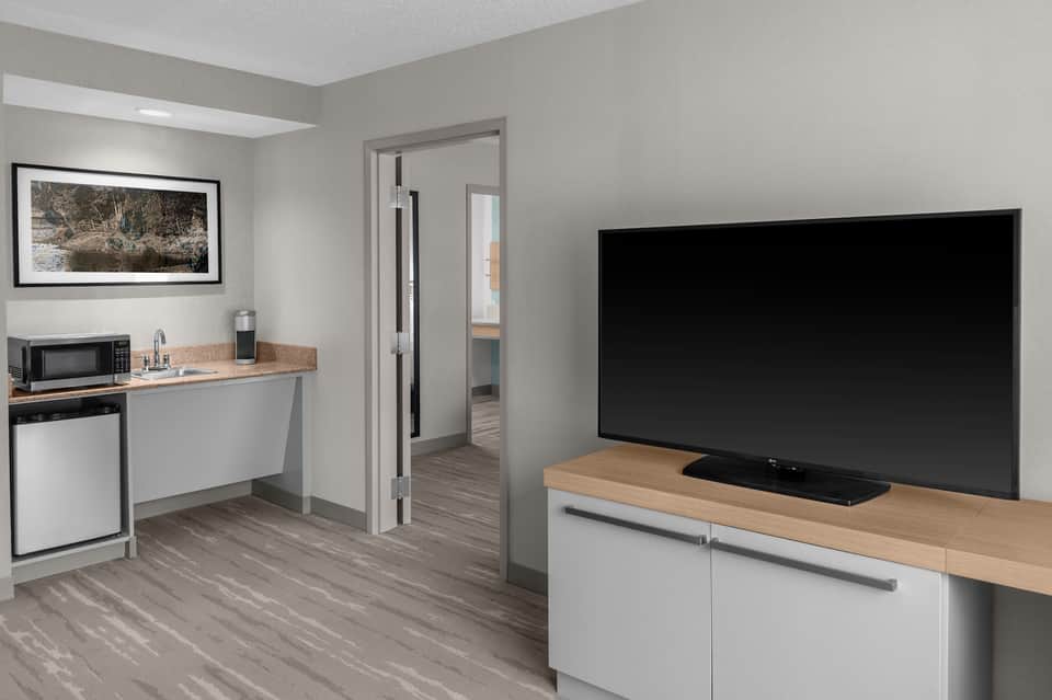 Hotel suite kitchenette with microwave, sink, and flat-screen TV mounted above wooden counter