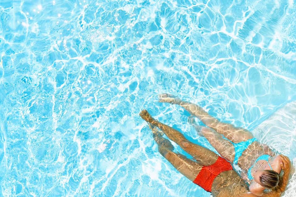Woman swimming in clear blue pool water wearing red swimsuit