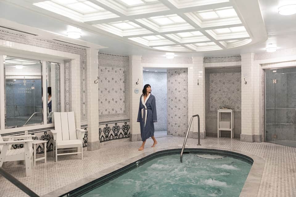 Elegant indoor spa with soaking tub, multiple shower stalls, white ceiling, and natural lighting