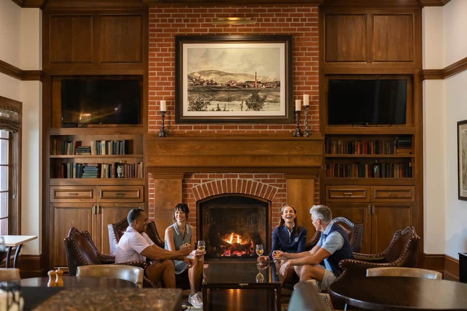 Group of people enjoying drinks by fireplace in elegant lounge with wood paneling and bookshelves