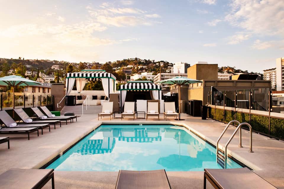 Rooftop pool with turquoise water, white cabanas with striped awnings, and city skyline views
