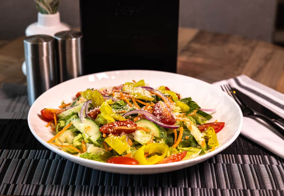 Colorful vegetable salad with mixed greens, peppers, carrots, and sesame seeds on white plate