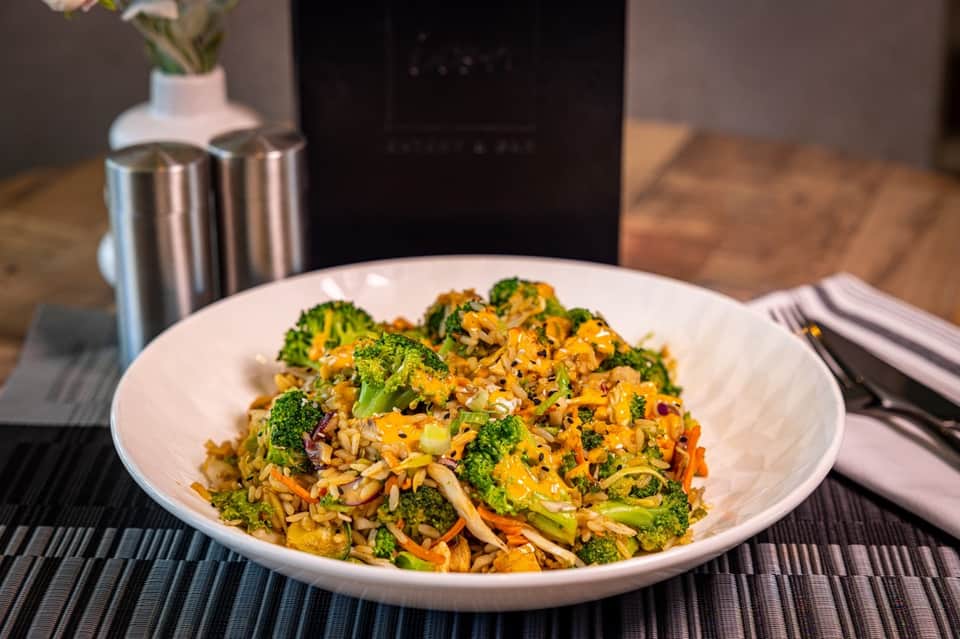 Colorful stir-fried broccoli and vegetables with crispy noodles served on white plate