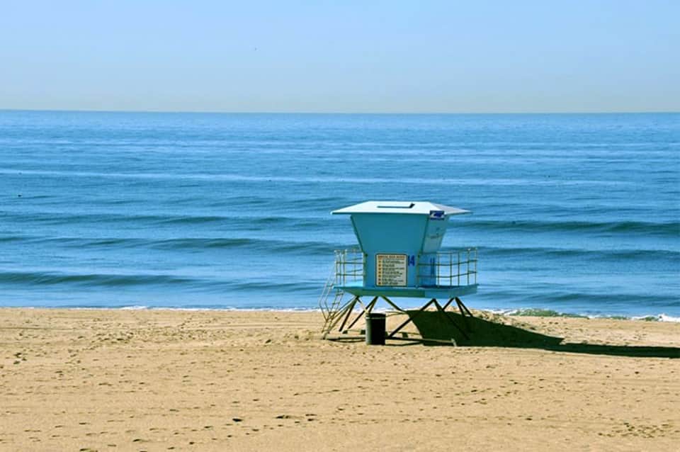 Turquoise lifeguard tower on sandy beach with calm blue ocean and clear sky