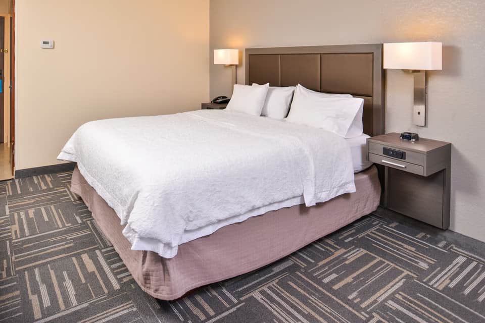 Single queen bed with white bedding in a hotel room with brown headboard and geometric patterned carpet