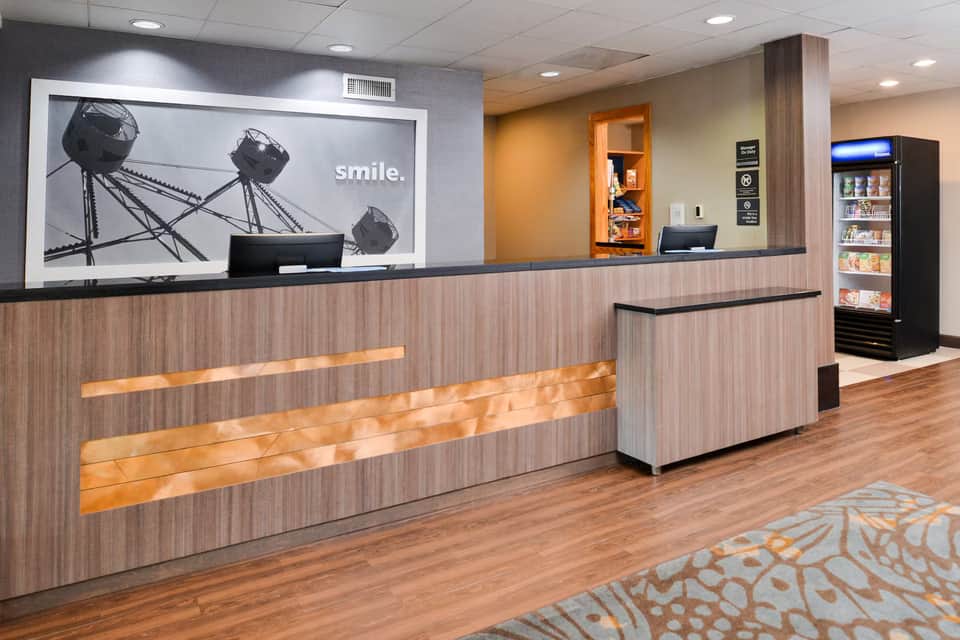 Hotel front desk with wooden paneling, inspirational wall art, and a beverage cooler in the lobby