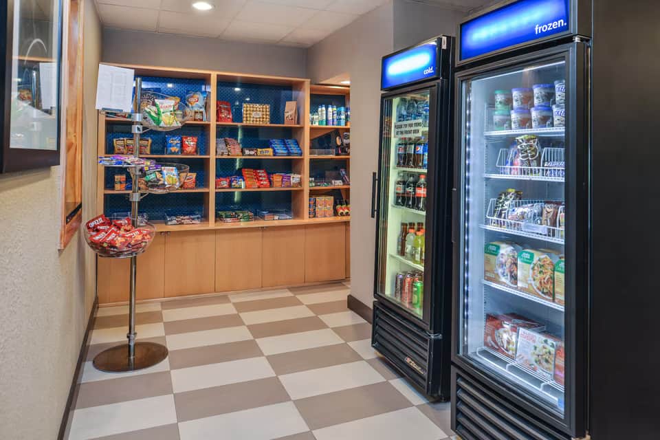 Hotel snack shop with wooden shelving displaying packaged items and refrigerated beverage and frozen food coolers