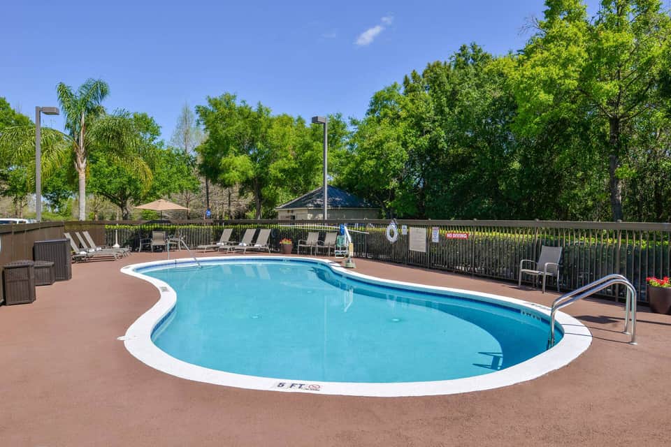 Resort swimming pool with white trim, lounge chairs, umbrellas, and lush landscaping in background