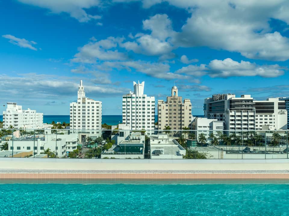 Beachfront Miami hotel skyline with Art Deco buildings, turquoise ocean, and white sandy beach under blue sky