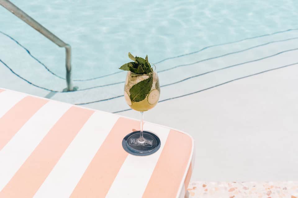 Mojito cocktail with mint and lime on striped beach lounger overlooking swimming pool