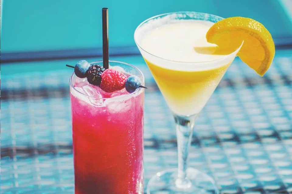 Tropical cocktails by the pool: pink berry drink with straw and yellow lemon martini with garnish