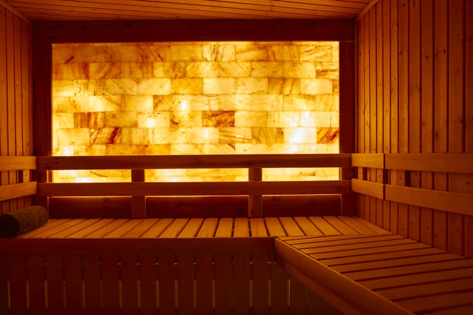Wooden sauna interior with glowing salt brick wall and wooden benches