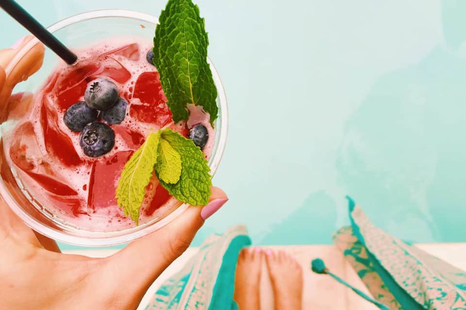 Pink berry cocktail with fresh blueberries and mint leaves in tropical setting
