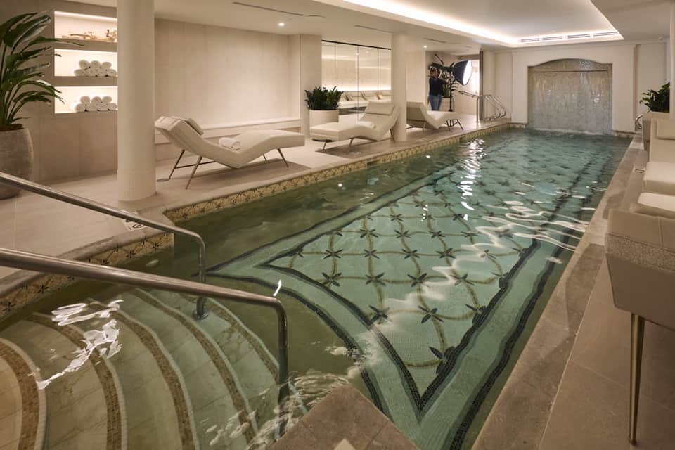 Indoor spa pool with decorative green tile floor and modern lounge chairs