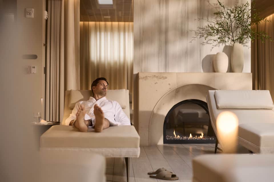 Man relaxing on bed in luxury hotel room with fireplace and floor-to-ceiling windows