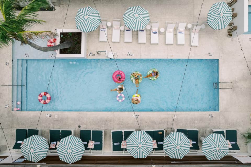 Overhead view of rectangular pool with swimmers on floats, green-striped umbrellas, and loungers