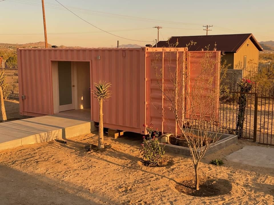 Rust-colored shipping container structures with desert landscaping and mountains in background