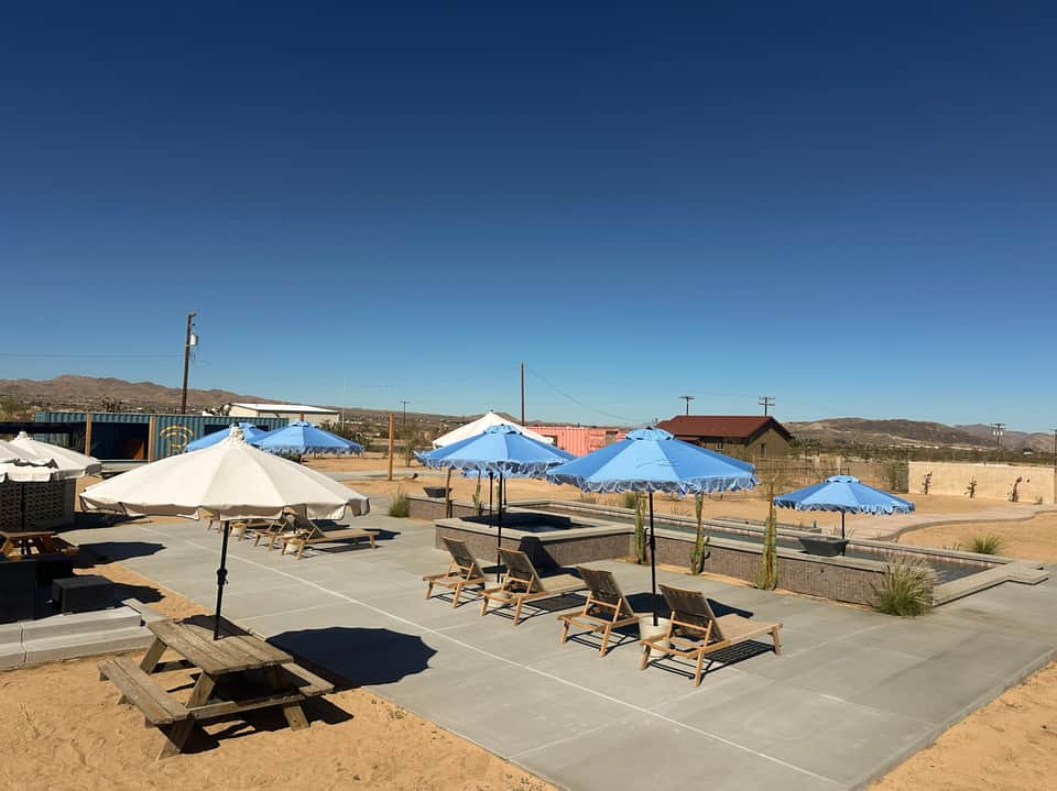 Resort pool deck with blue and white umbrellas, lounge chairs, and desert mountain views