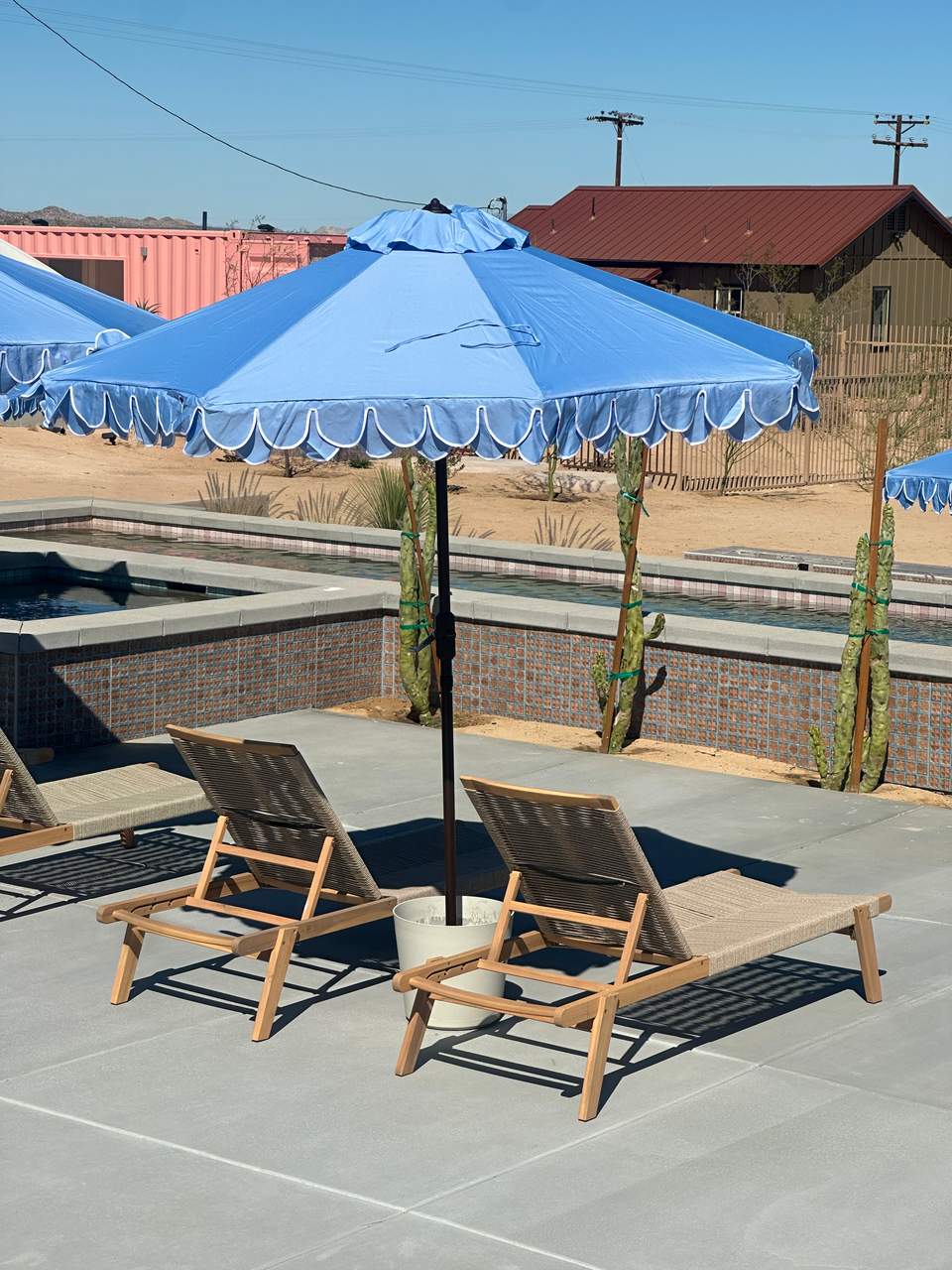 Single blue umbrella over two wooden lounge chairs beside a brick-lined pool