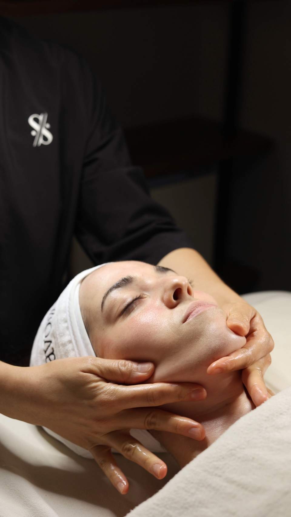 Facial massage treatment with hands on client's face wearing white headband