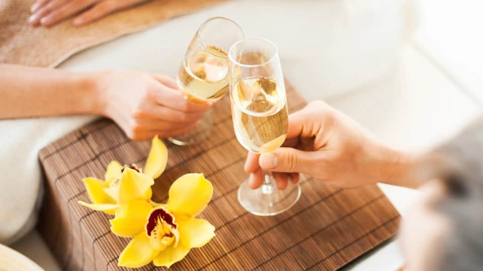 Two people toasting with champagne glasses beside a yellow orchid flower on a wooden table