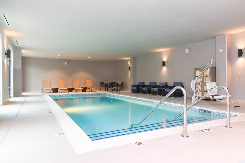Indoor lap pool with lane markers, handrails, lounge chairs, and modern architectural design