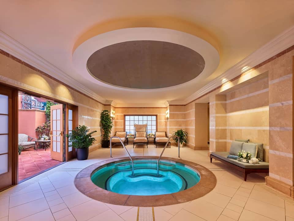 Luxurious indoor spa with circular hot tub, beige marble walls, skylights, and access to terrace seating