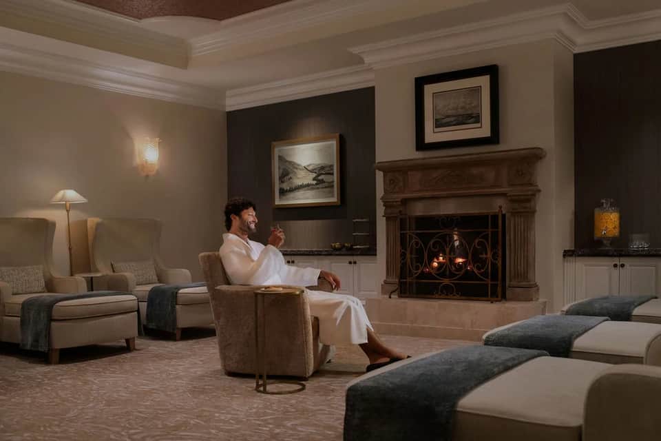 Luxury spa relaxation lounge with fireplace, seated guest in white robe, elegant furnishings and soft lighting