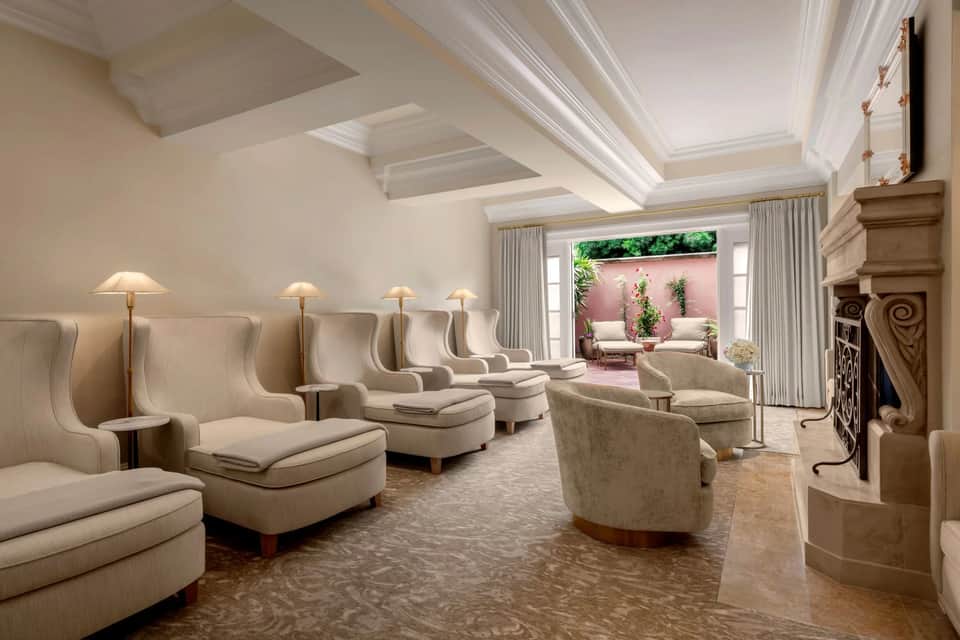 Spa relaxation room with rows of cream-colored wingback chairs, coffered ceiling, fireplace, and garden view