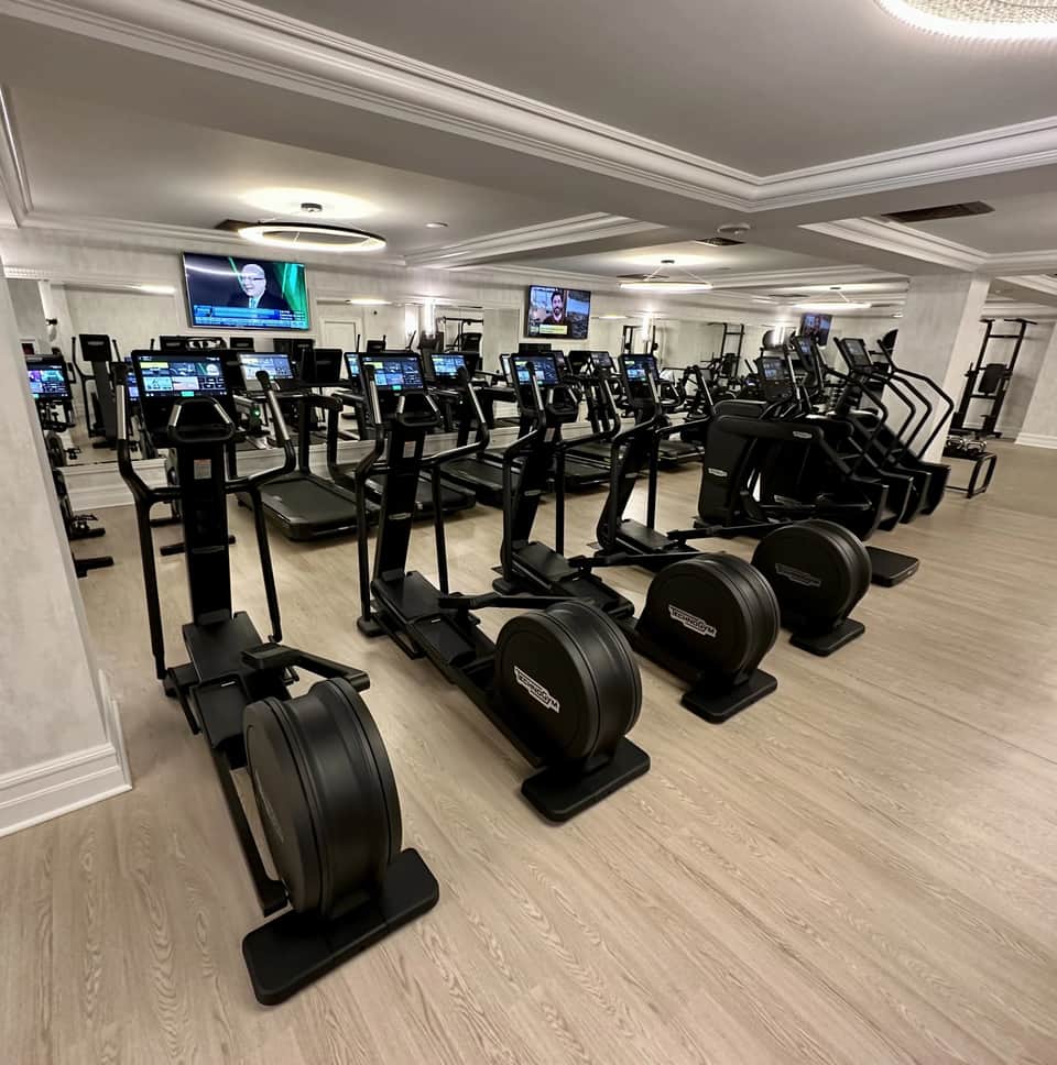 Modern fitness center with rows of stationary bikes and cardio equipment, flat-screen monitors, bright ceiling