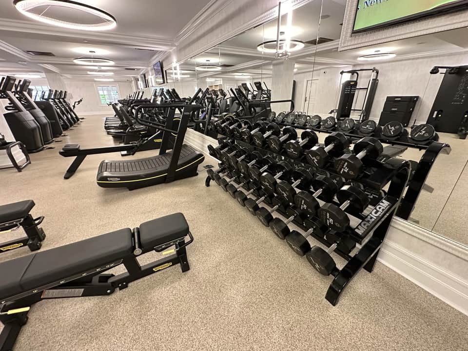 Luxury fitness facility with dumbbell rack, treadmills, and strength training equipment in bright, modern space