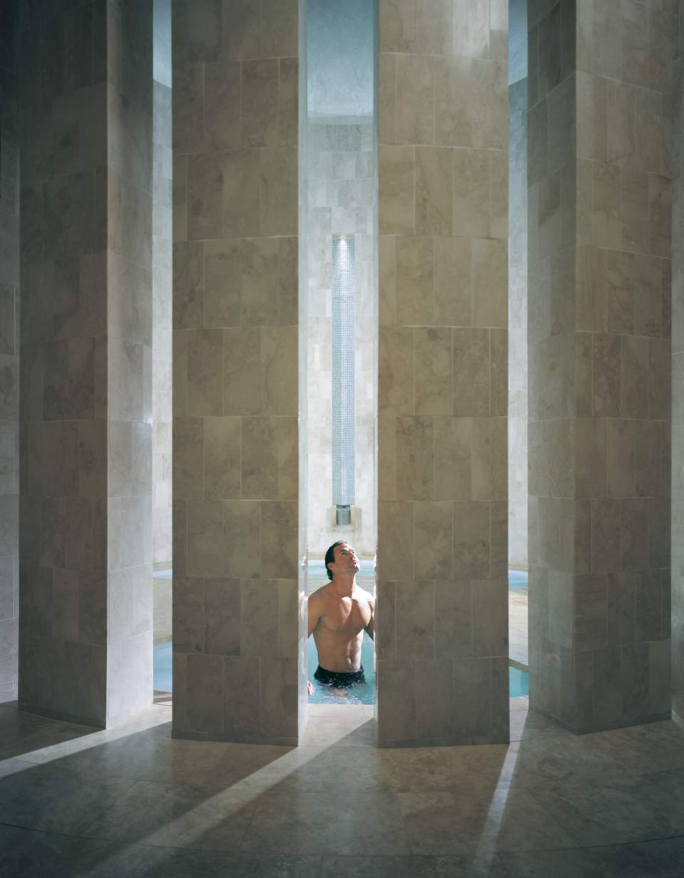 Man in swimming pool viewed through modern archways with green stone tile walls and natural light
