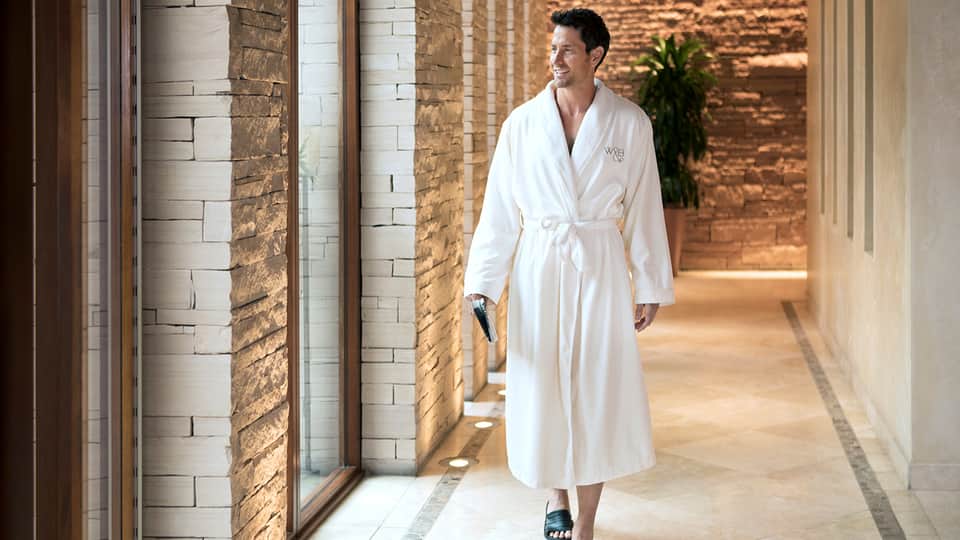 Man in white spa robe walking through contemporary corridor with brick and white stone architectural elements