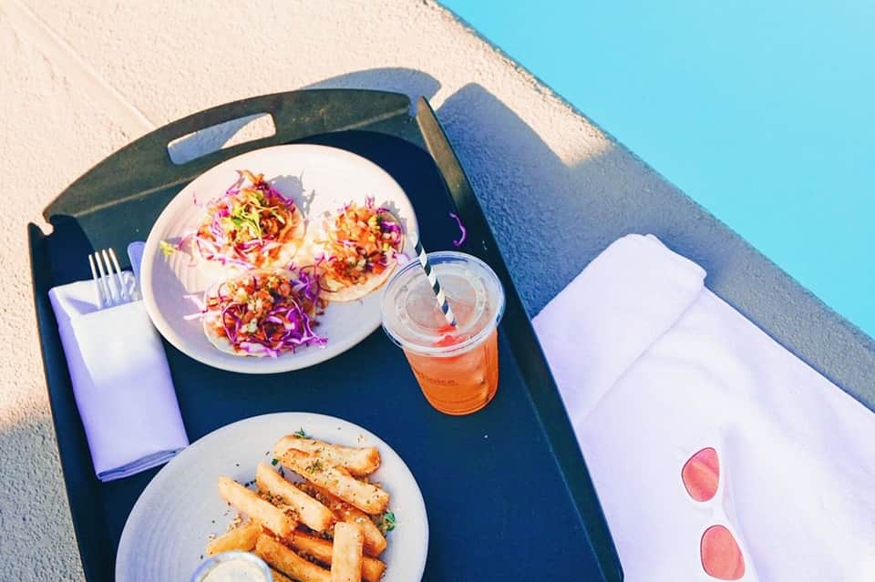 Beach lunch tray with colorful tacos, fries, and an orange beverage under blue sky