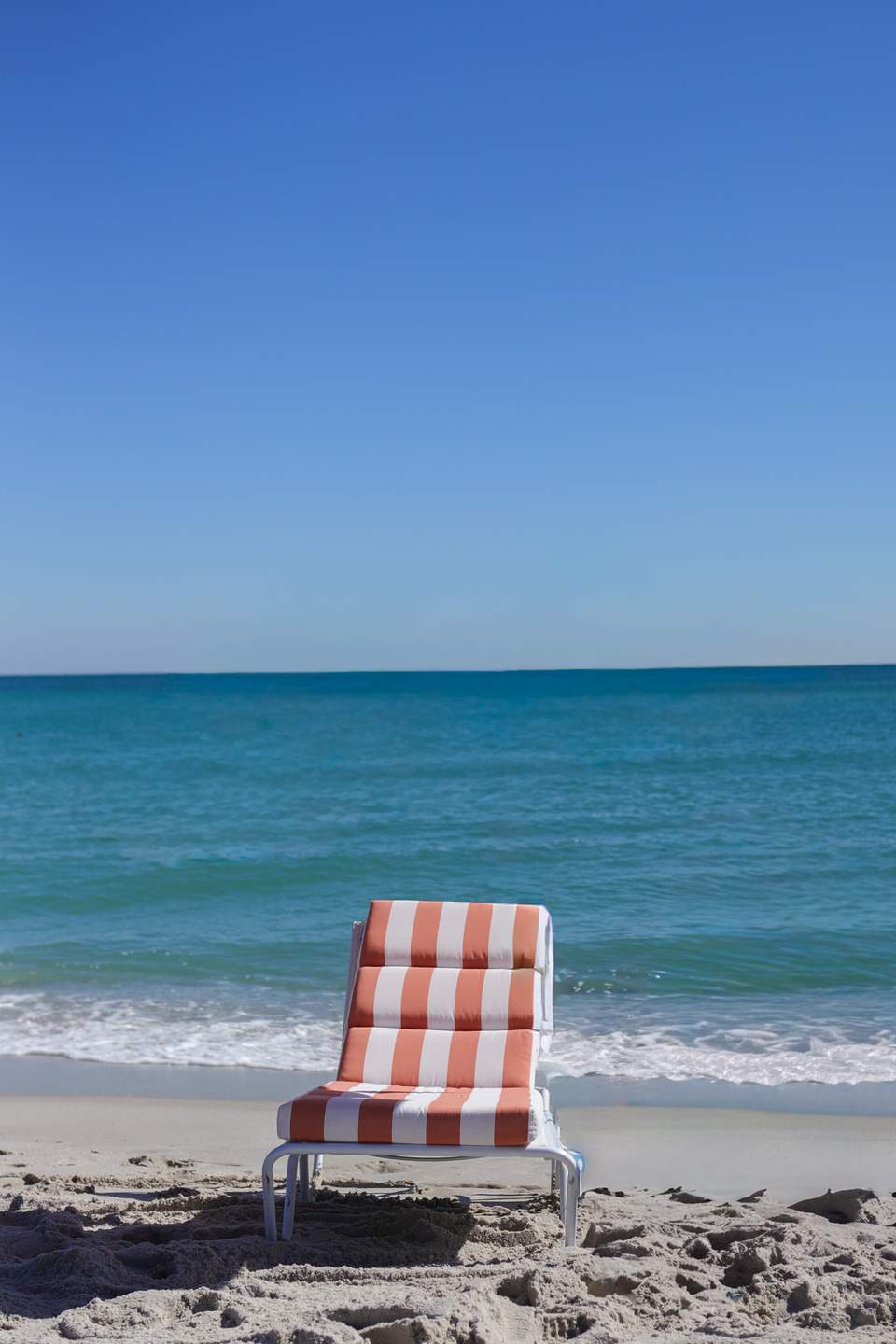 Red and white striped beach lounger facing the ocean with waves in background