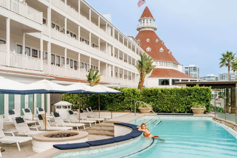 Resort pool with loungers and umbrellas, historic red-roofed hotel building in background