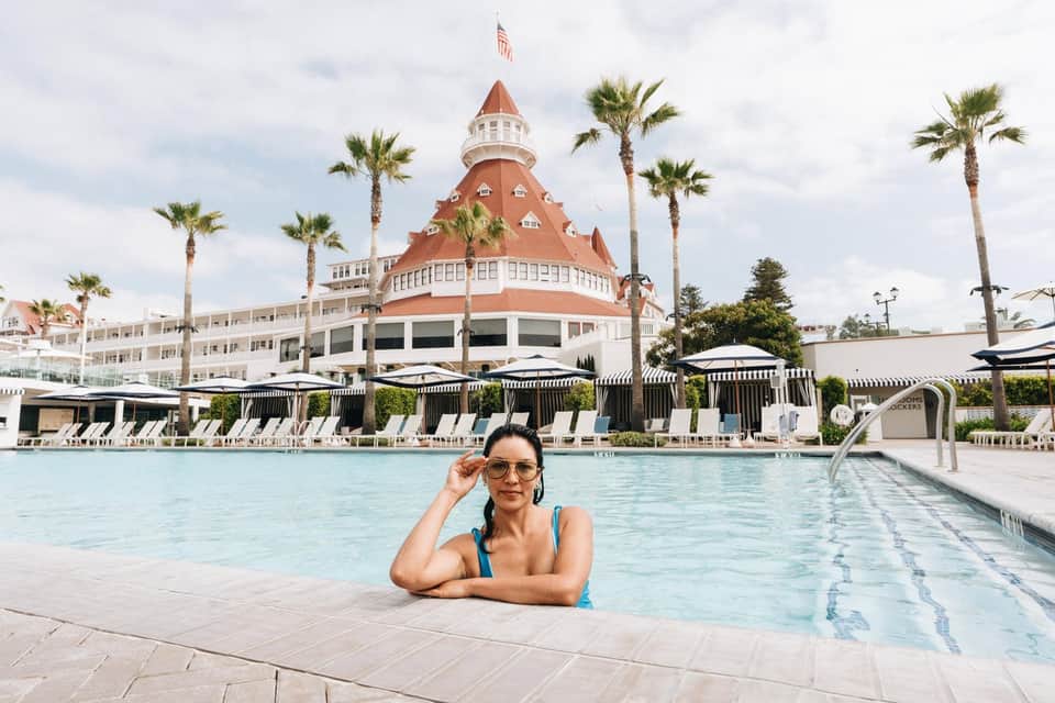 Woman in pool at resort with distinctive red-roofed Victorian hotel tower and palm trees behind