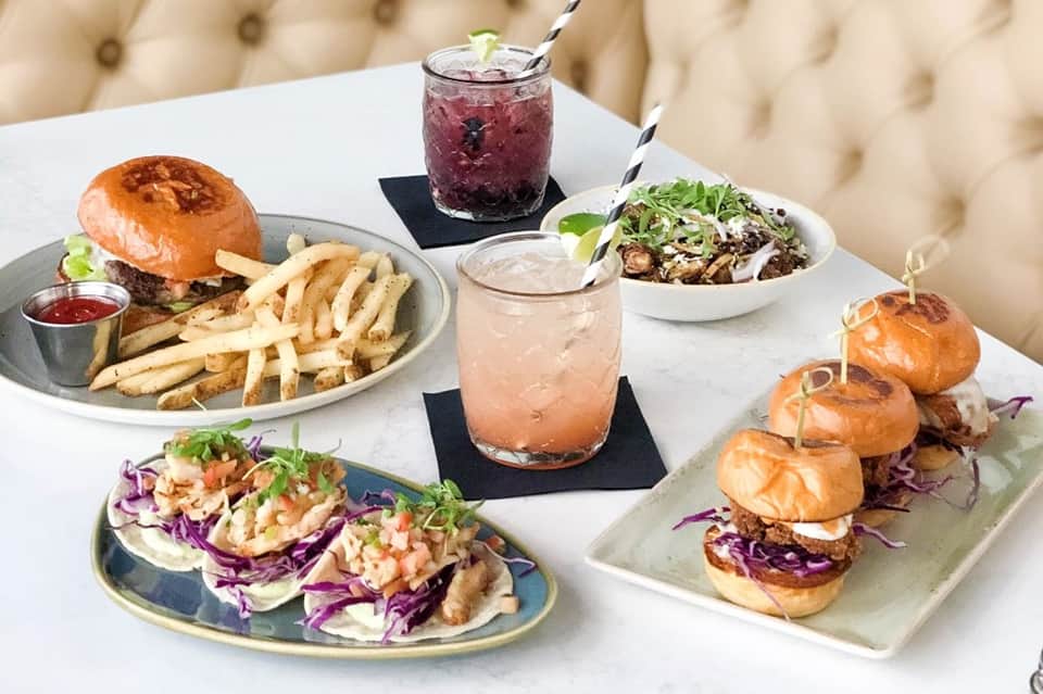 Restaurant table with burgers, fries, sliders, salads, and cocktails on white tablecloth
