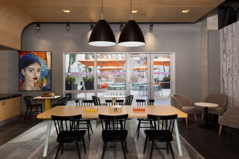 Modern dining area with large windows, wooden table, black pendant lights, and colorful artwork overlooking outdoor terrace