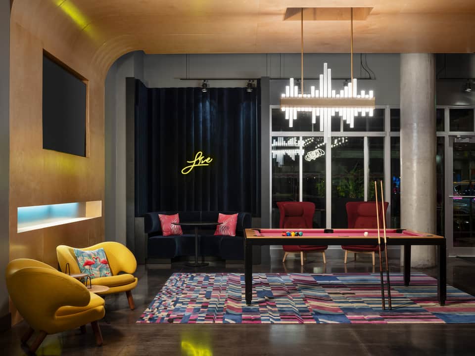 Contemporary entertainment lounge with yellow chair, red pool table, neon signage, and acoustic elements