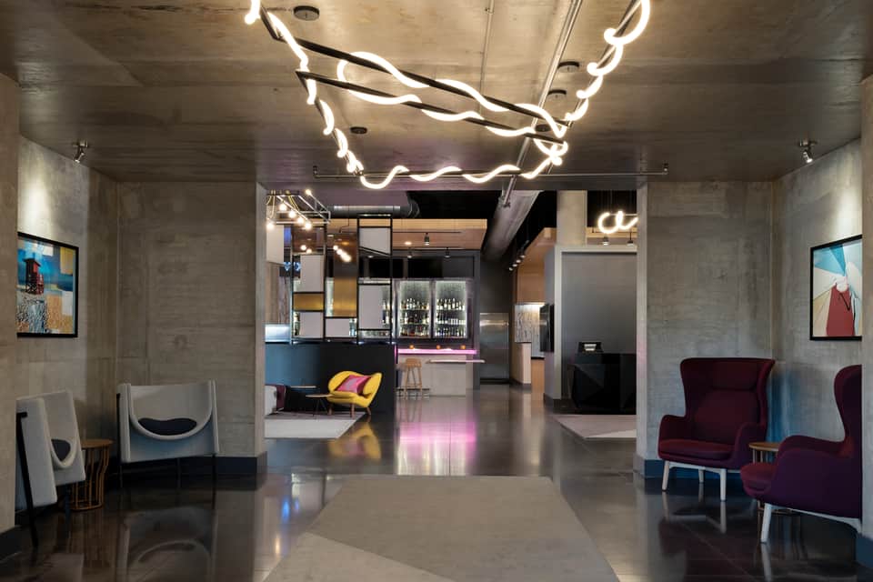 Urban hotel corridor with concrete walls, neon branch lighting, bar area, and modern furnishings