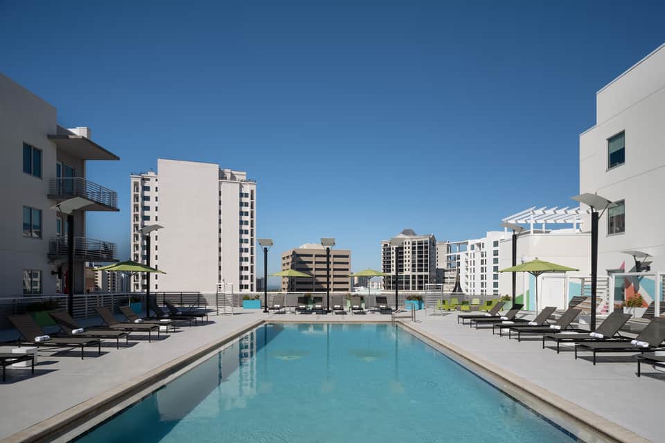 Rooftop swimming pool with lounge chairs, green umbrellas, and surrounding apartment buildings